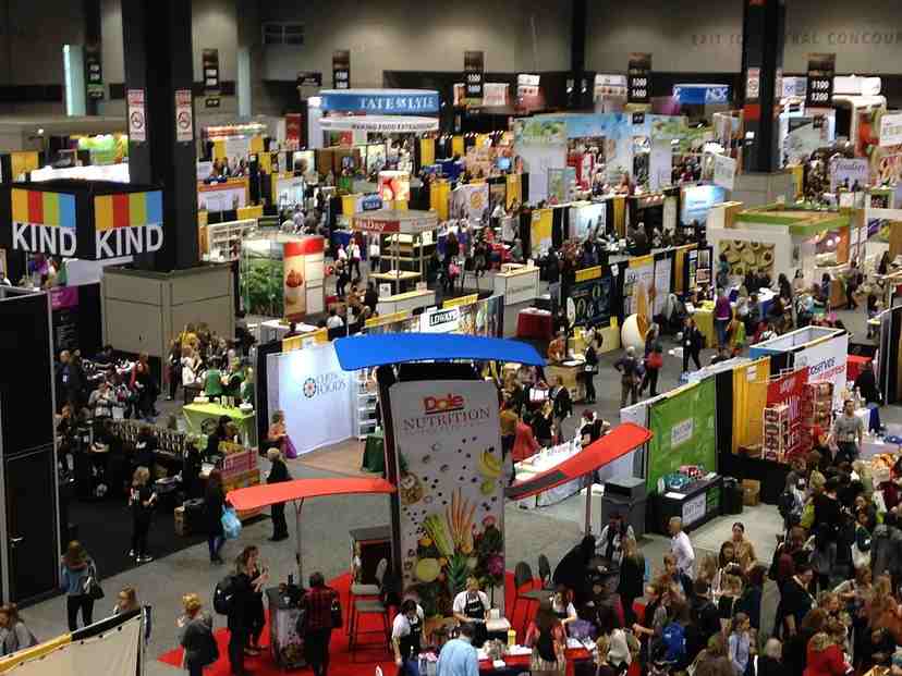 The image shows several startup kiosks in a hall where people are interacting and promoting their business
