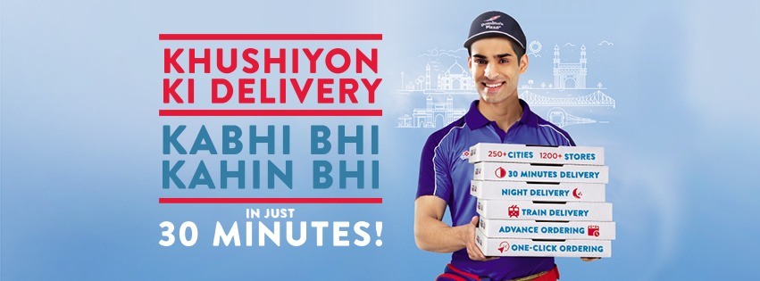 This image shows an ad campaign by Domino’s with a man standing with pizza boxes