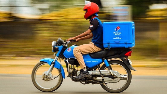 This image shows a delivery boy on his way to deliver Pizza on the Domino’s scooter